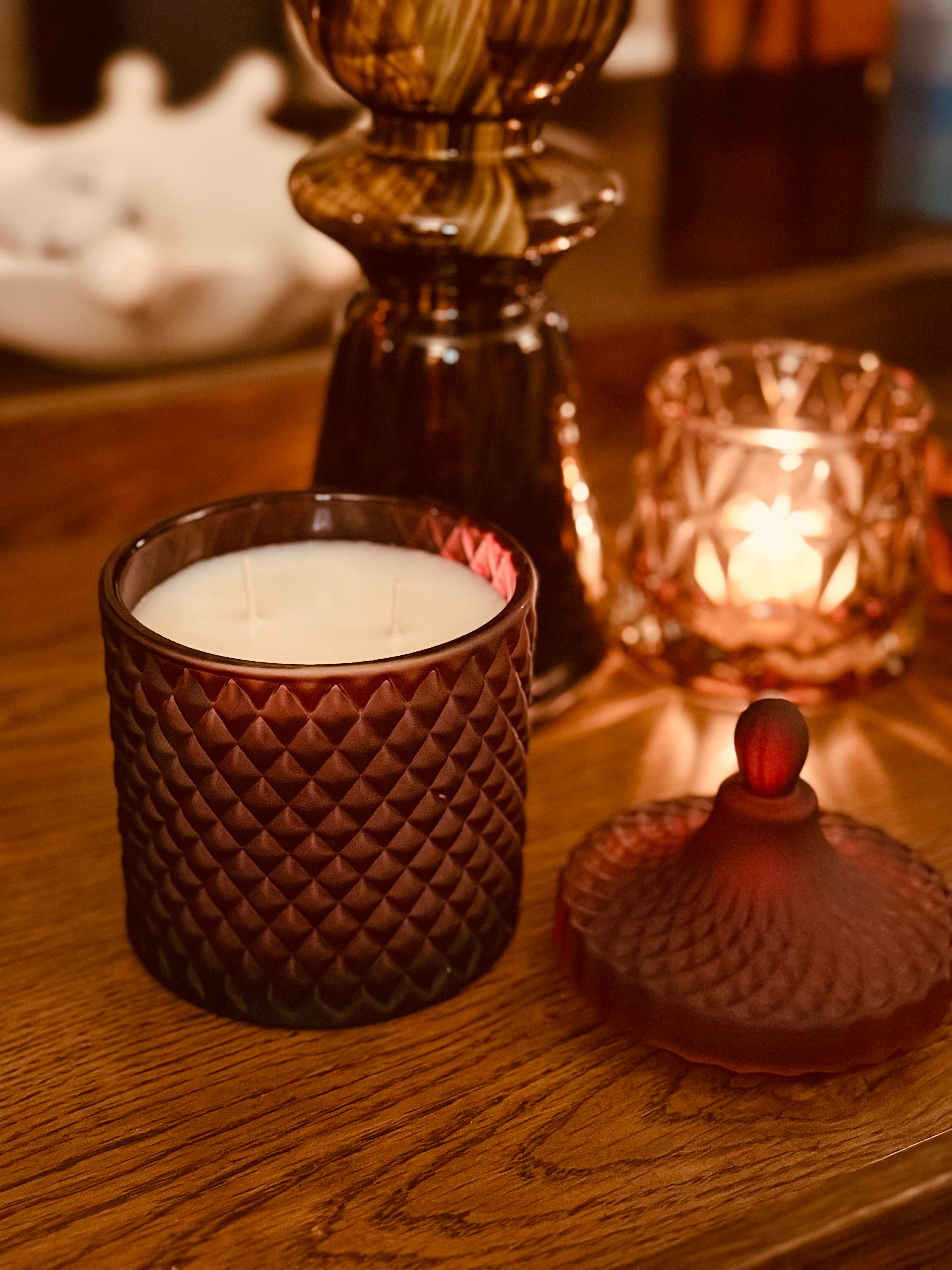 Decorative candle in a textured glass holder on a wooden surface with a warm glow.