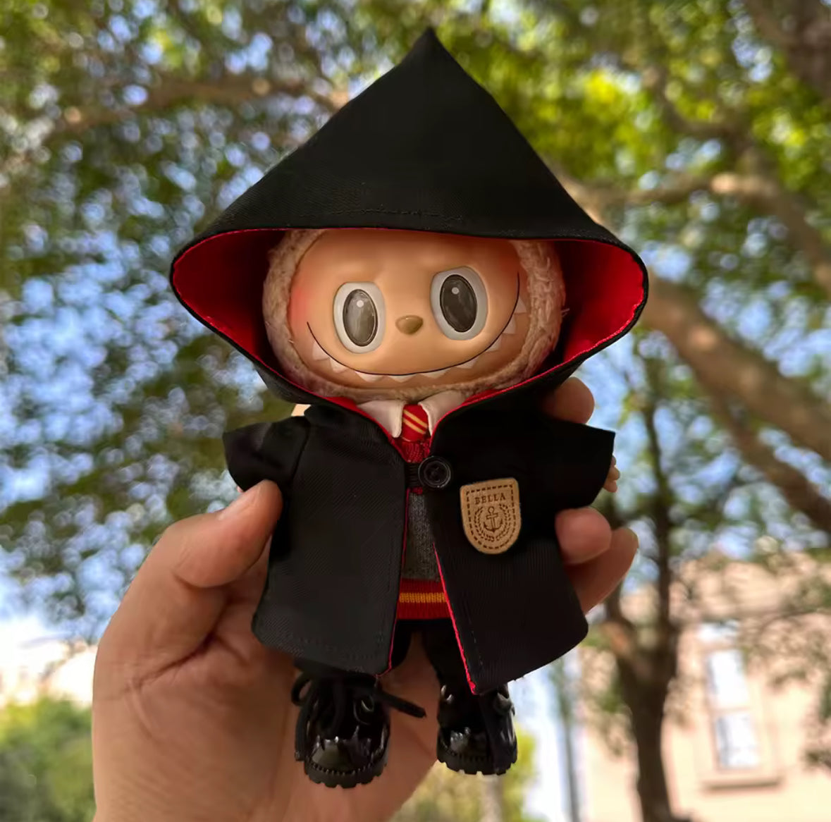 Harry Potter Clothing set for Labubu Doll, in a black hood and coat held by a hand with a blurred natural background