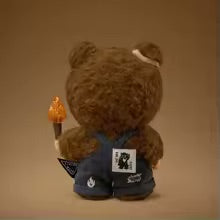 Brown teddy bear with a lit candle and a small sign on a brown background