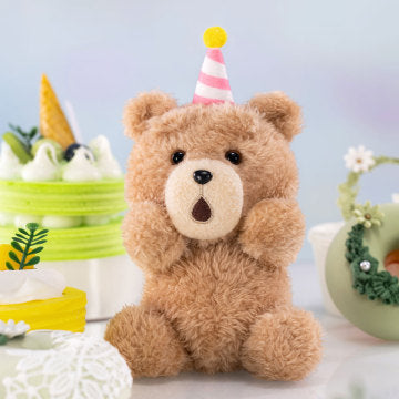 Teddy bear wearing a party hat on a decorative table with small plants and a colorful background