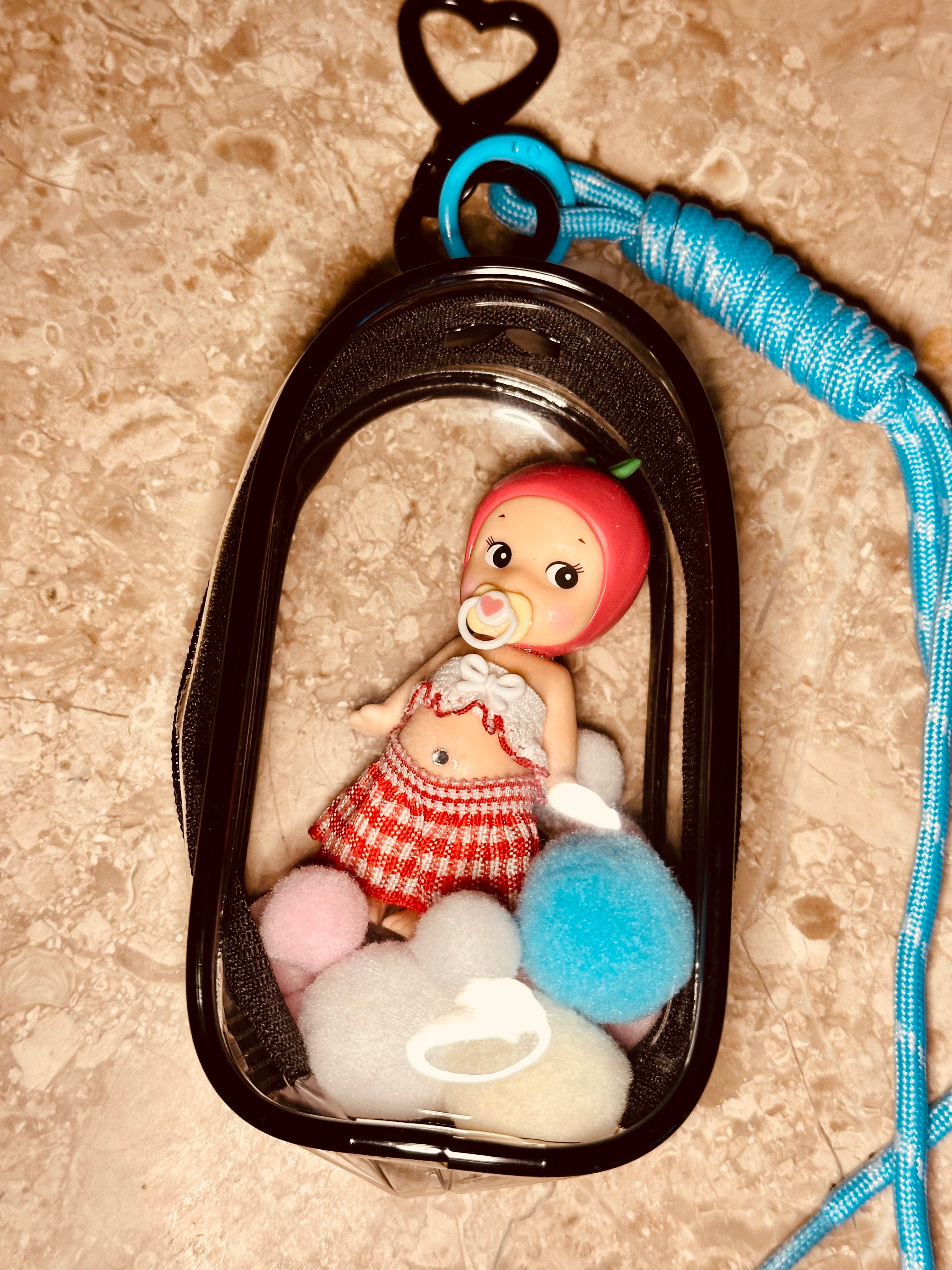 Small figurine of a child with a pacifier inside a clear container on a textured surface.