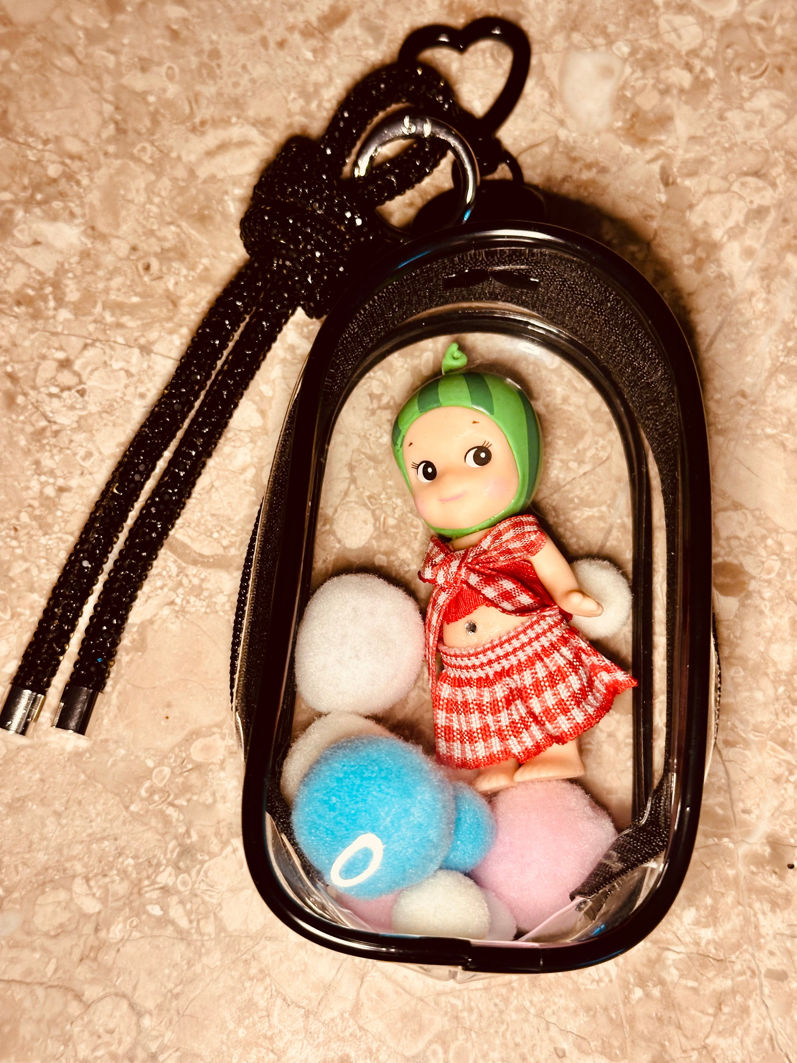 Keychain with a small doll and colorful balls inside a black case on a beige surface.