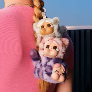 Plush keychain shaped like three cartoon characters on a person's pink sleeve with a blue sky background.