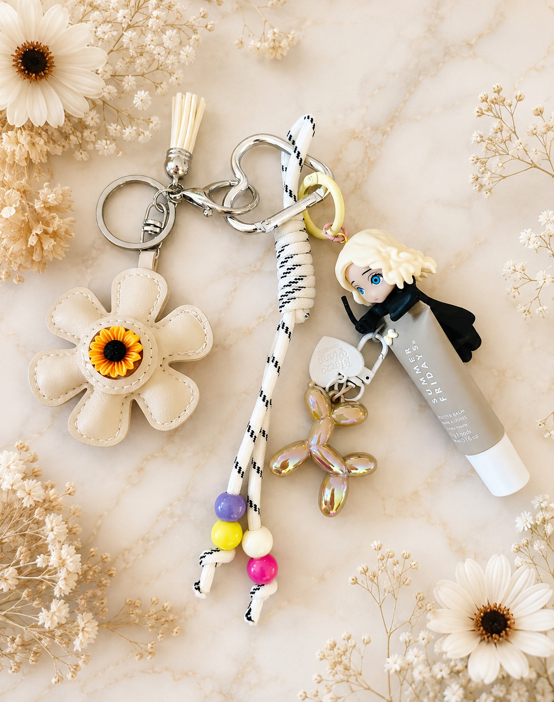 Customised bag charm featuring a Draco Malfoy-inspired figure in black robes with braided rope, colourful beads, sunflower daisy charm, gold balloon dog charm and Summer Fridays Lip Butter in Vanilla