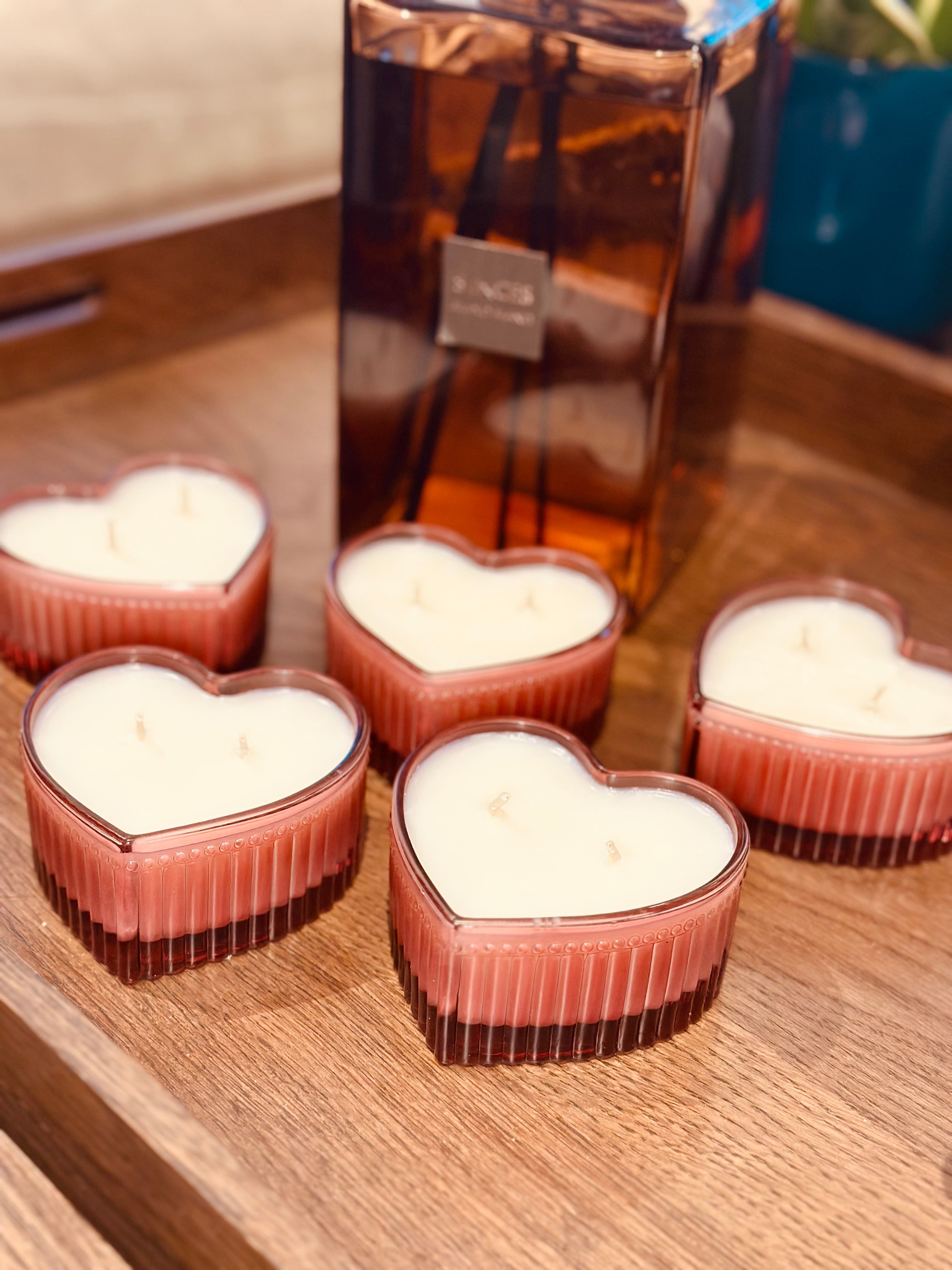 Heart-shaped candles on a wooden surface with a bottle in the background