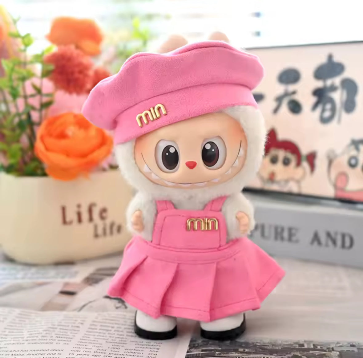 Labubu figure wearing a pink outfit with 'min' branding on a surface with flowers in the background.