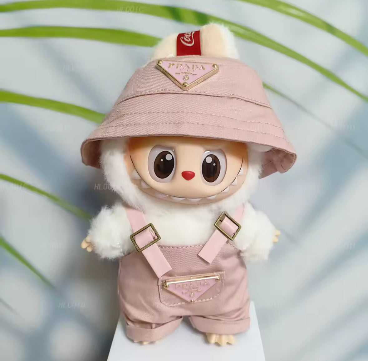 Labubu figure wearing a pink hat and overalls with a blurred green background
