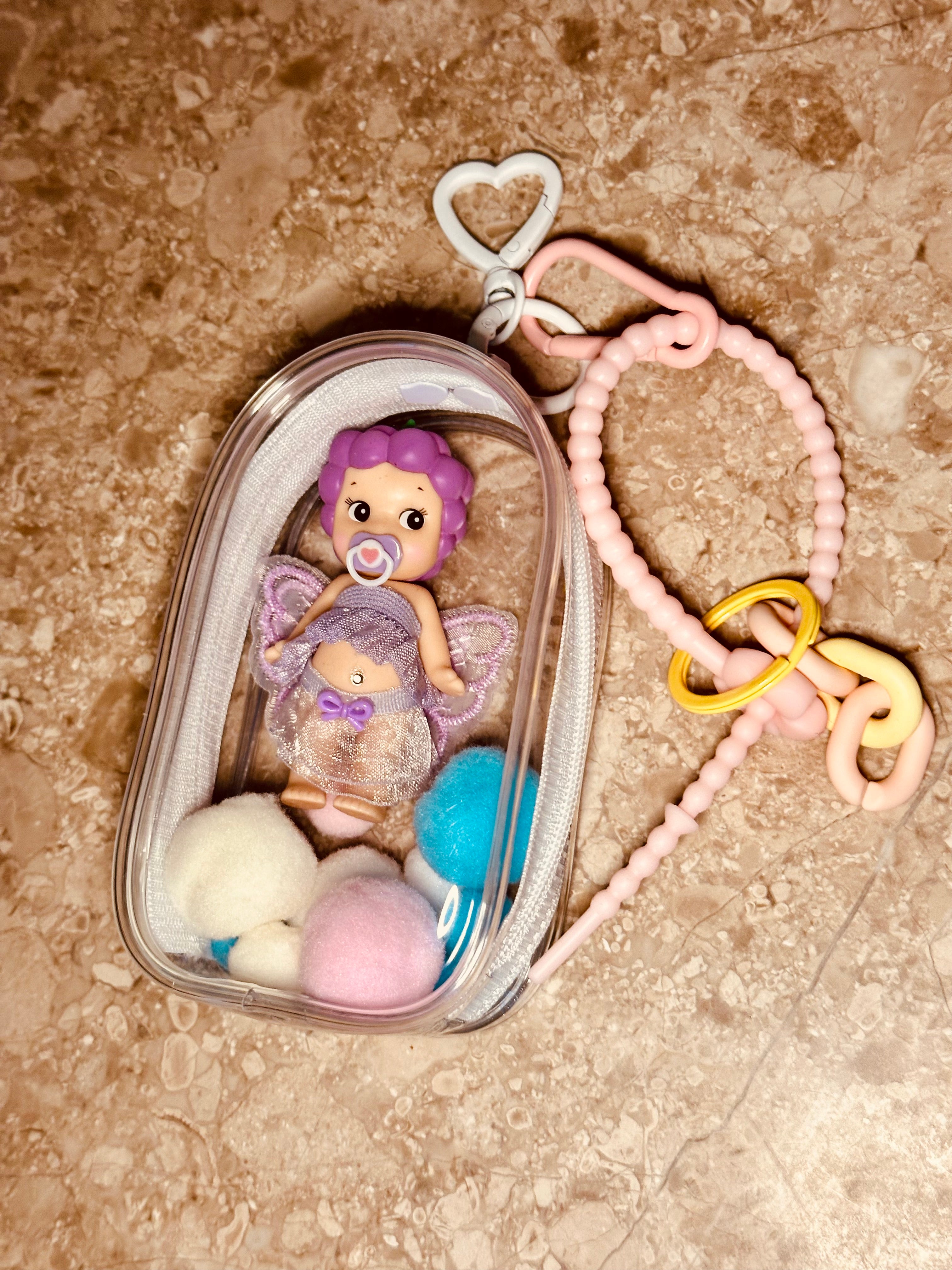 Baby doll with purple hair in a clear container on a textured surface