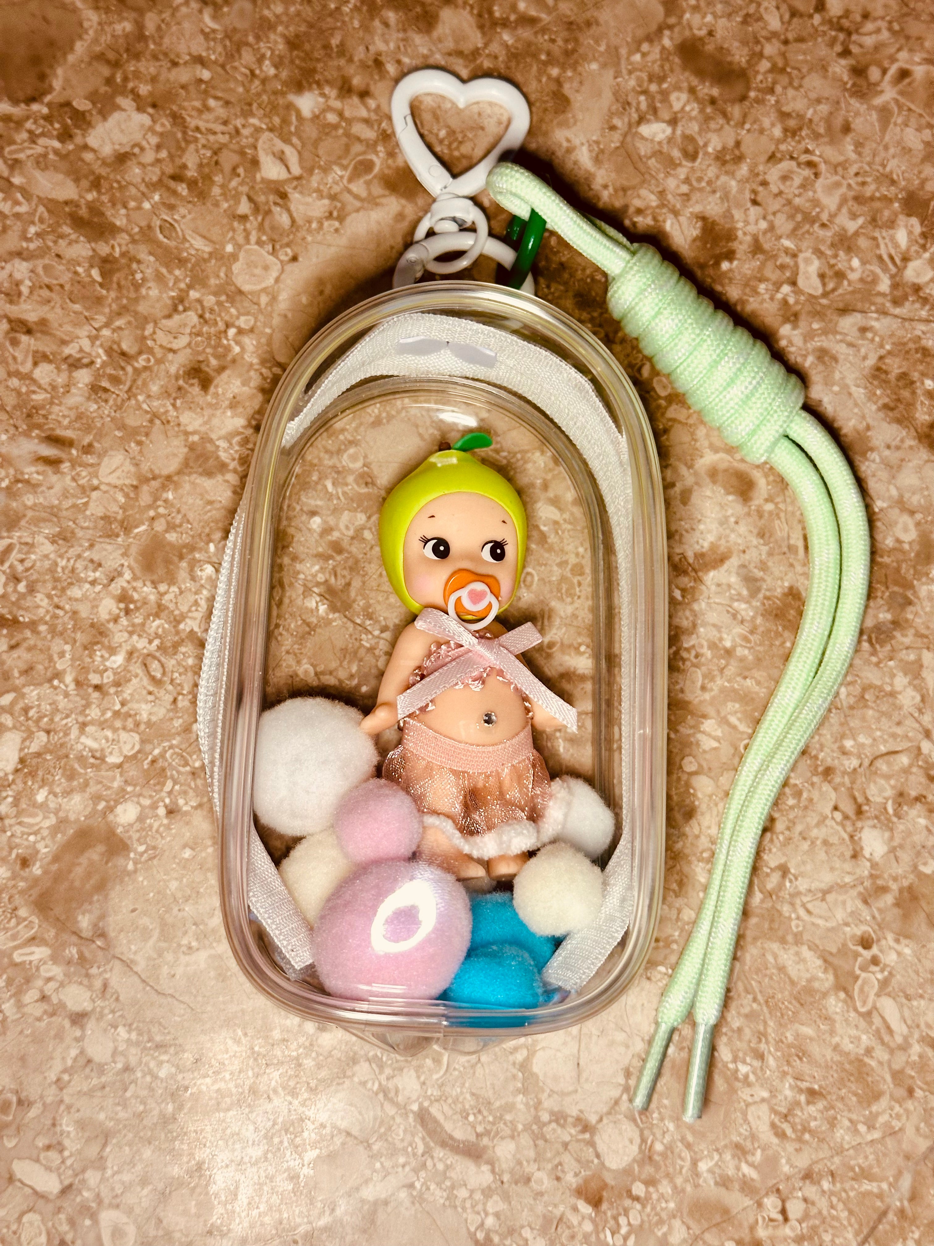 Small toy baby in a clear container with colorful balls on a textured surface
