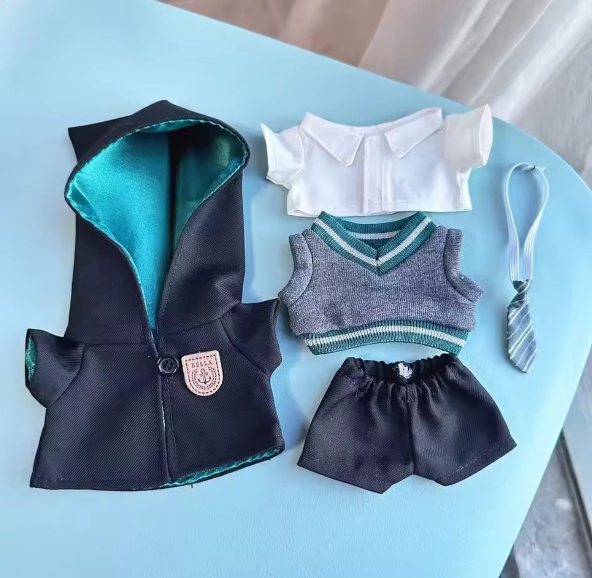 Set of Labubu Doll clothing including a black hooded jacket, white shirt with collar, gray sweater vest, black shorts, and a striped tie on a light blue surface.