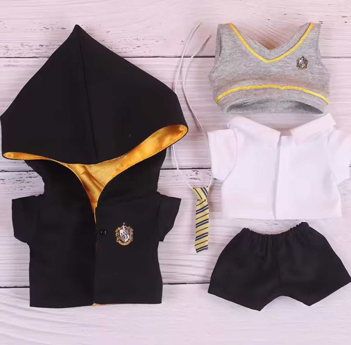 Black hoodie with gold lining, gray sports bra with yellow trim, white shirt, and black shorts on a light wooden surface.