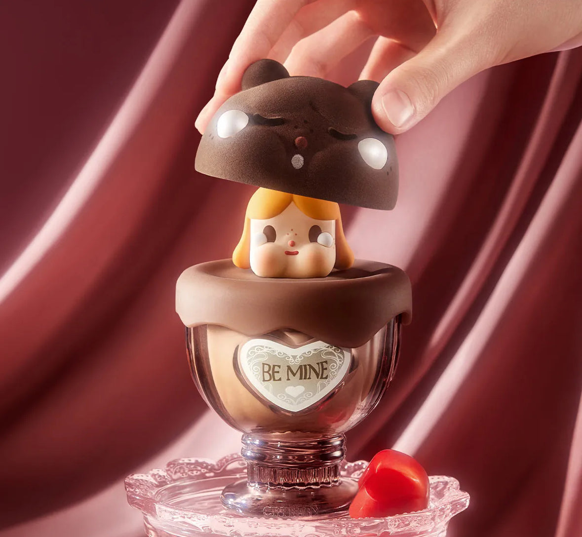 Chocolate figurine with a heart-shaped 'BE MINE' message on a pink background