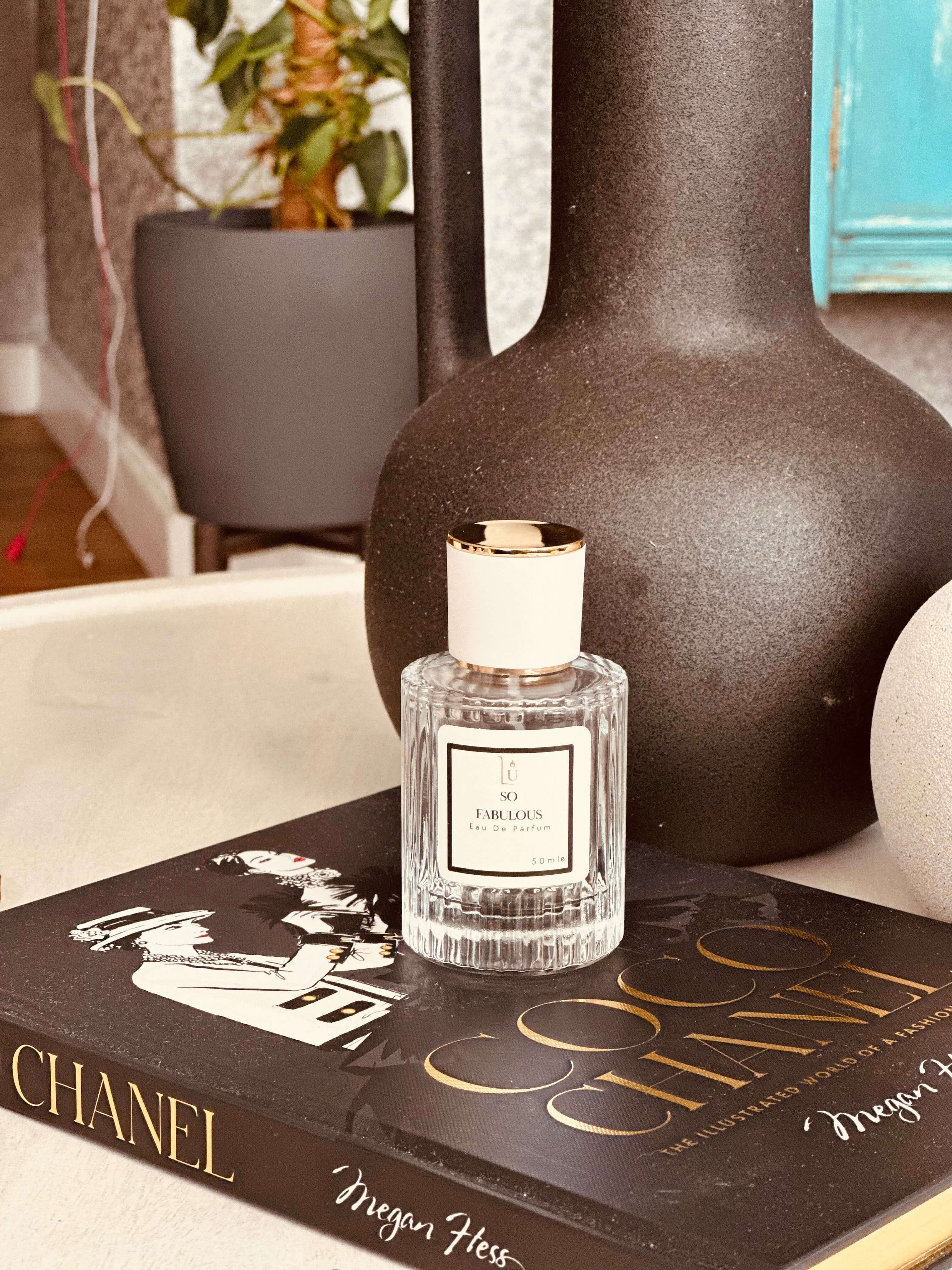 Cashmeran & Amber Eau de Parfum by LU Fragrances — 50ml glass bottle with white label and gold cap, styled on a Coco Chanel coffee table book with a large dark ceramic vase
