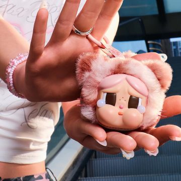 Small pink plush toy held in hands with a blurred background