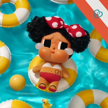 Toy figure of a character with a polka dot headband on a inflatable ring surrounded by pool toys.