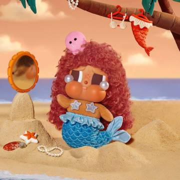 Mermaid toy with red hair and blue tail on a sandy beach with ocean view