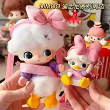 Two small plush toys resembling a duck with a bow, held by a person.