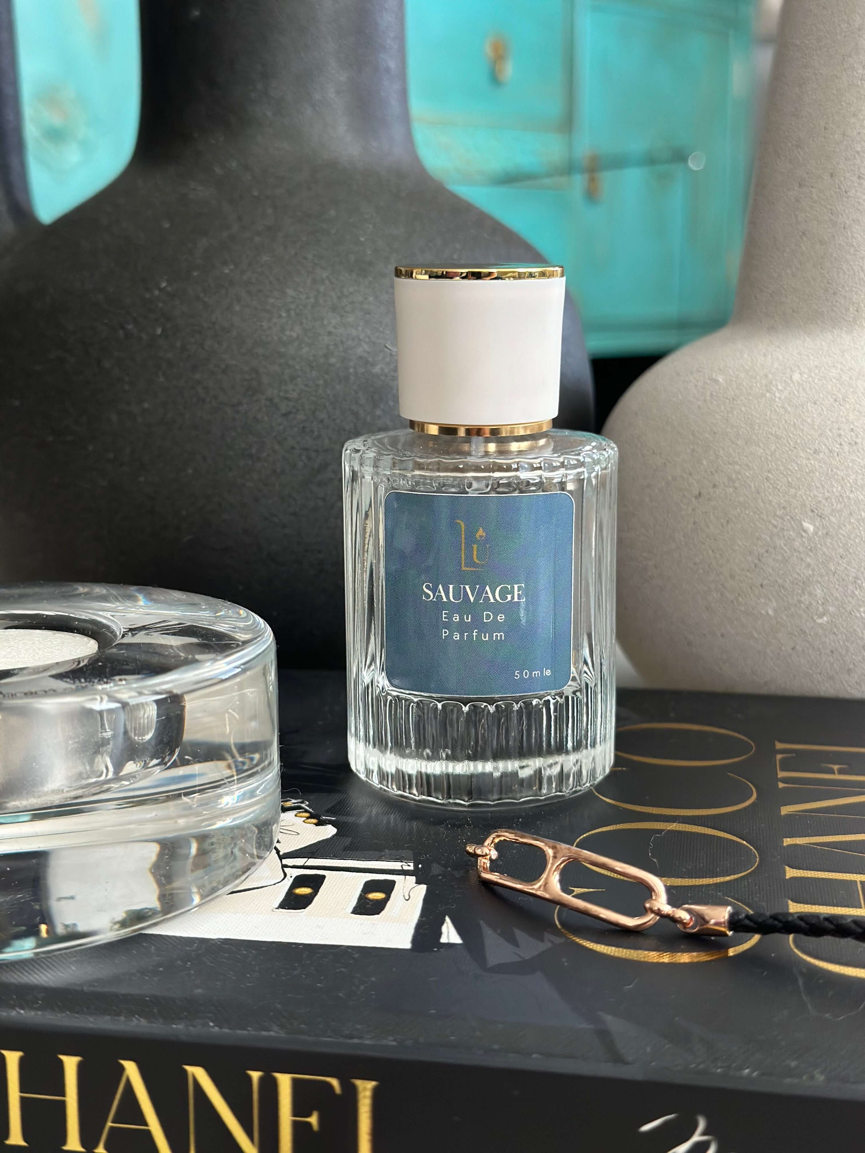 Fresh Bergamot & Ambroxan Eau de Parfum by LU Fragrances — 50ml bottle lying on its side on a fashion book, with dark and cream ceramic vases and a gold chain in the foreground

