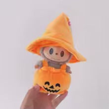 Stuffed toy in an orange pumpkin costume held by a hand on a white background