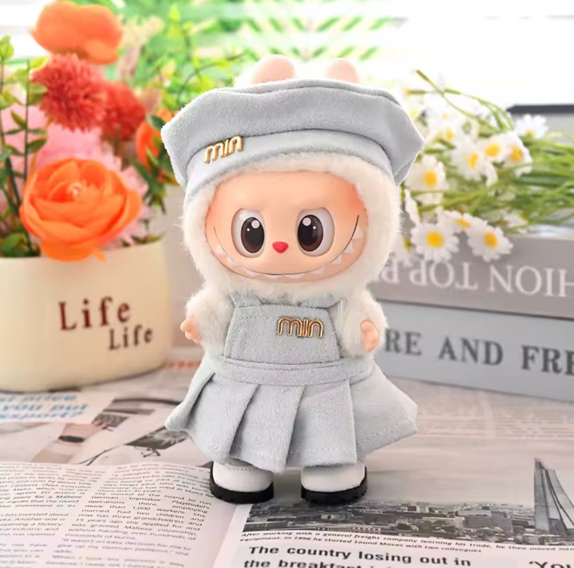 Labubu doll with a gray outfit and hat on an open book with flowers in the background