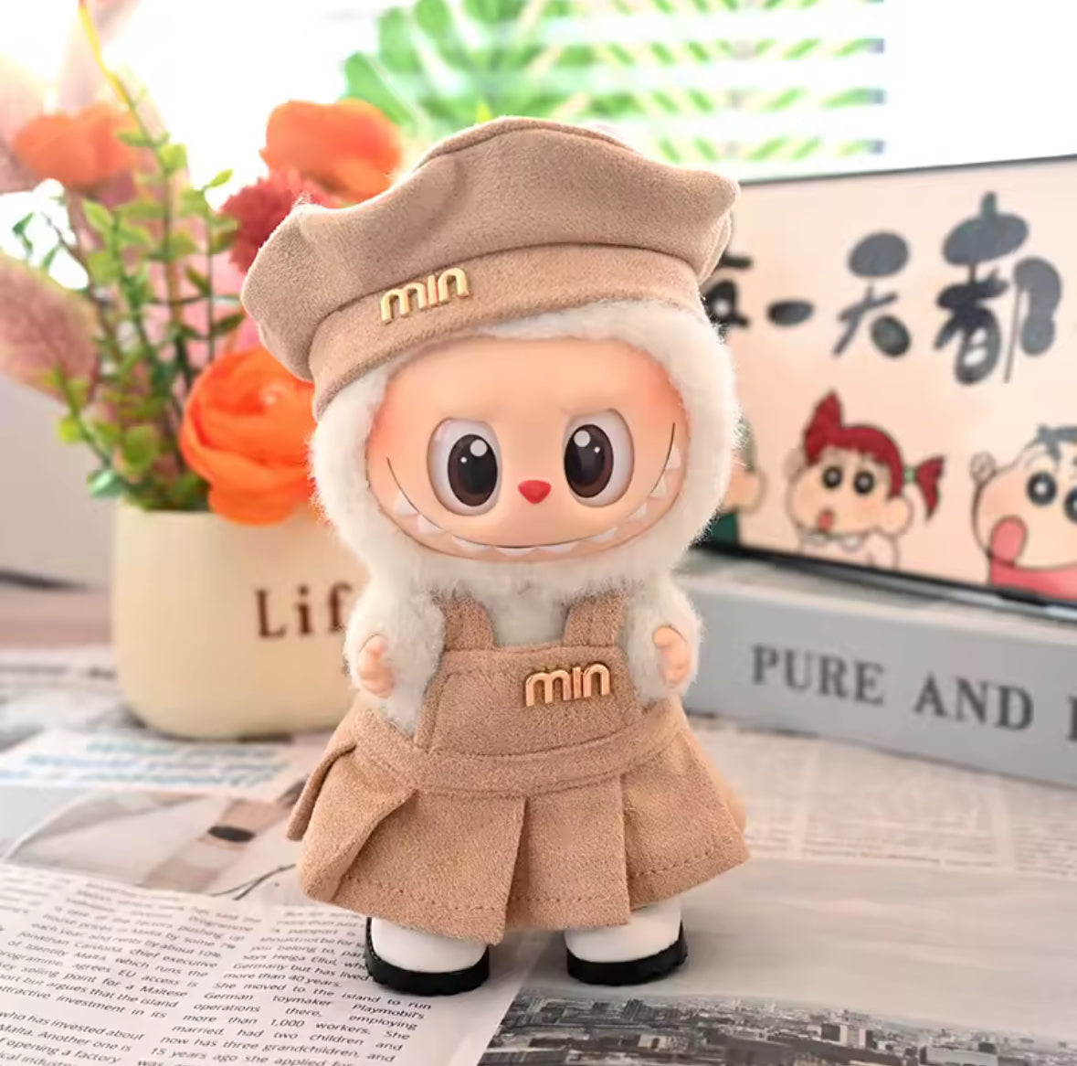 Labubu figure with a beige hat and skirt on a surface with a magazine and flowers in the background