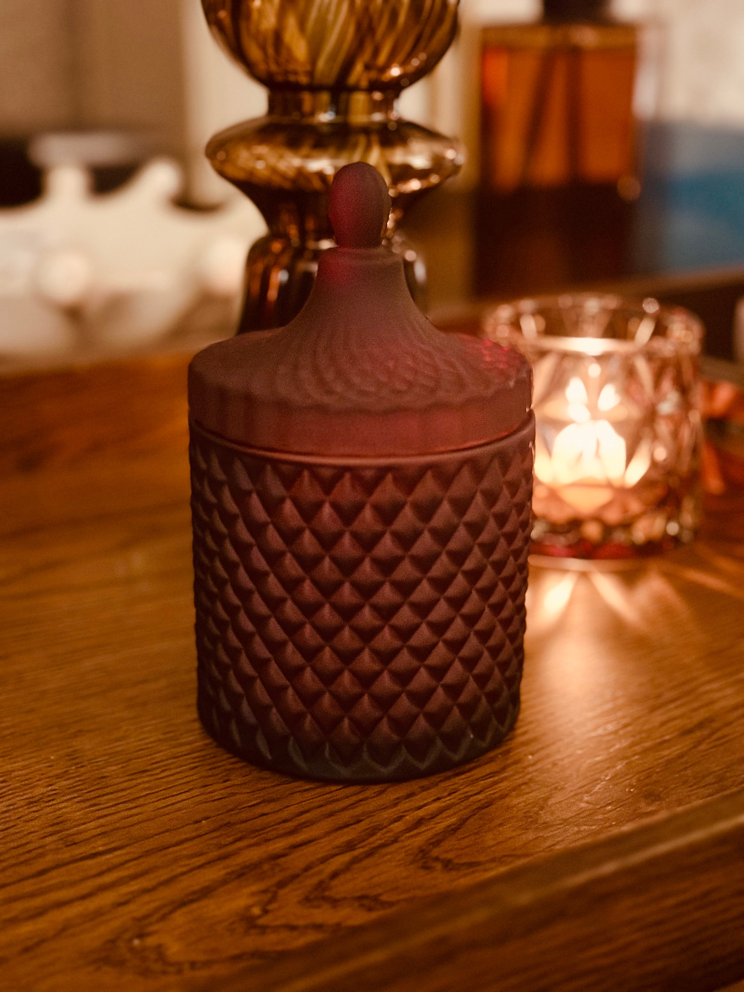 Textured Bohemian Midnight Red candle on a wooden surface with a blurred background