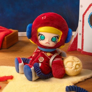 Plush toy with red helmet and outfit sitting on a surface with a blue wall and red object in the background
