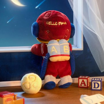 Red plush toy with 'Hello Mom' text, sitting on a table with educational blocks and a moon toy.
