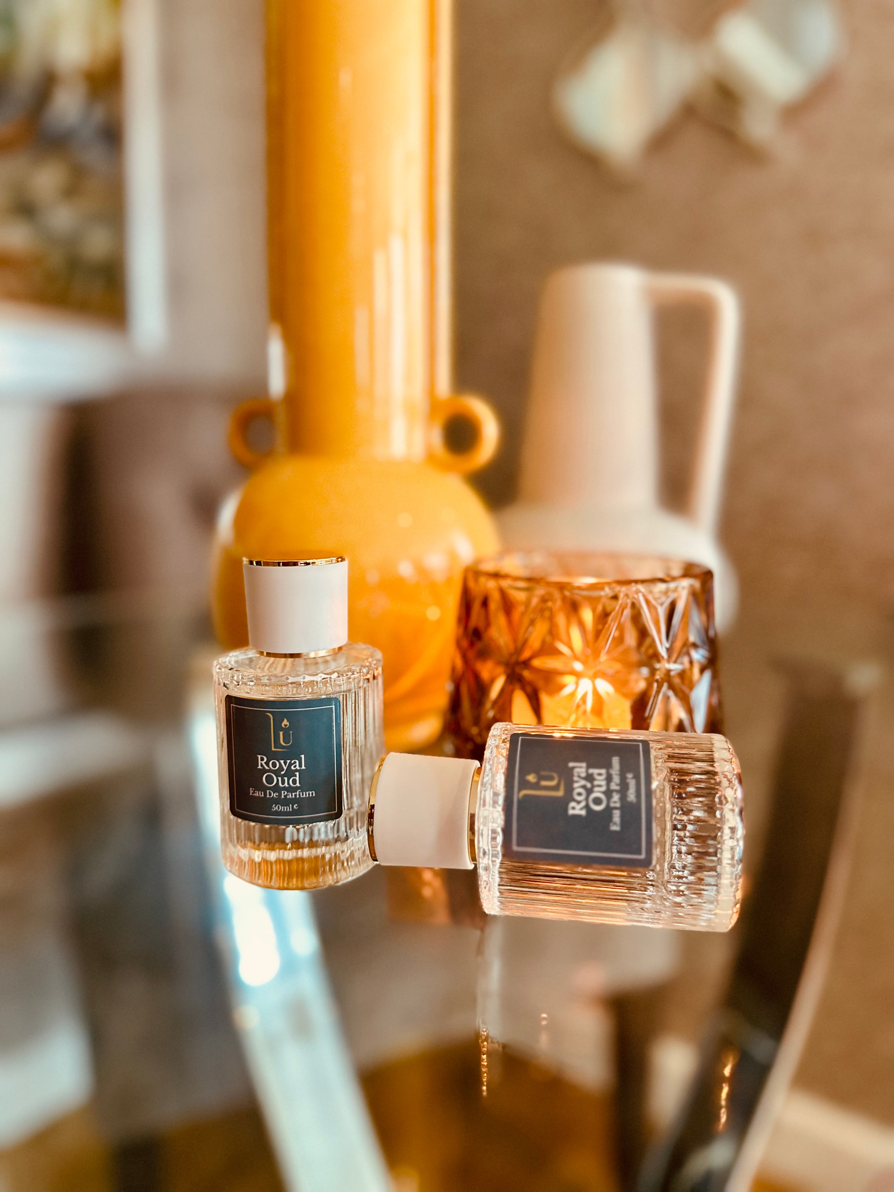 Oud & Bergamot Eau de Parfum by LU Fragrances — 50ml and 10ml bottles on a glass surface with amber candle and yellow vase