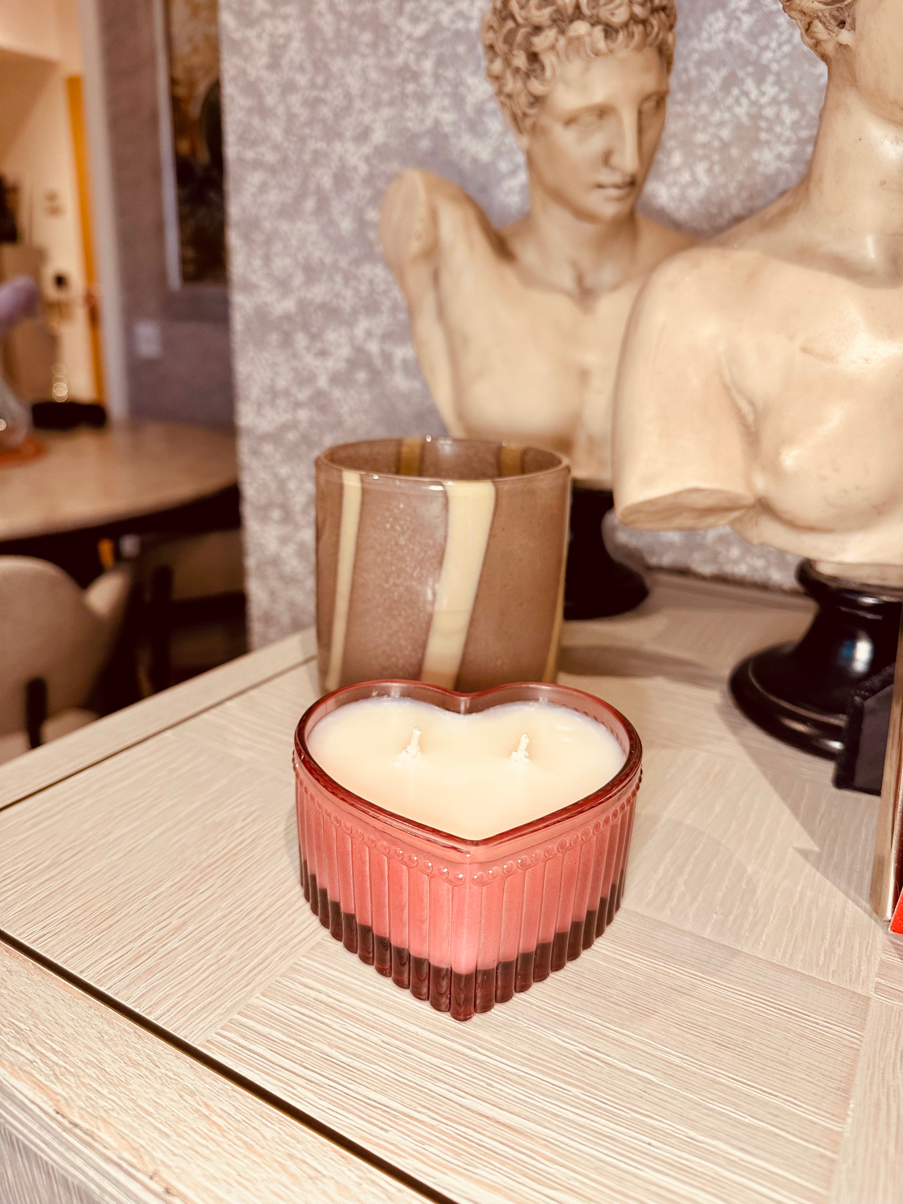 Heart-shaped candle in a decorative holder on a table with classical statues in the background