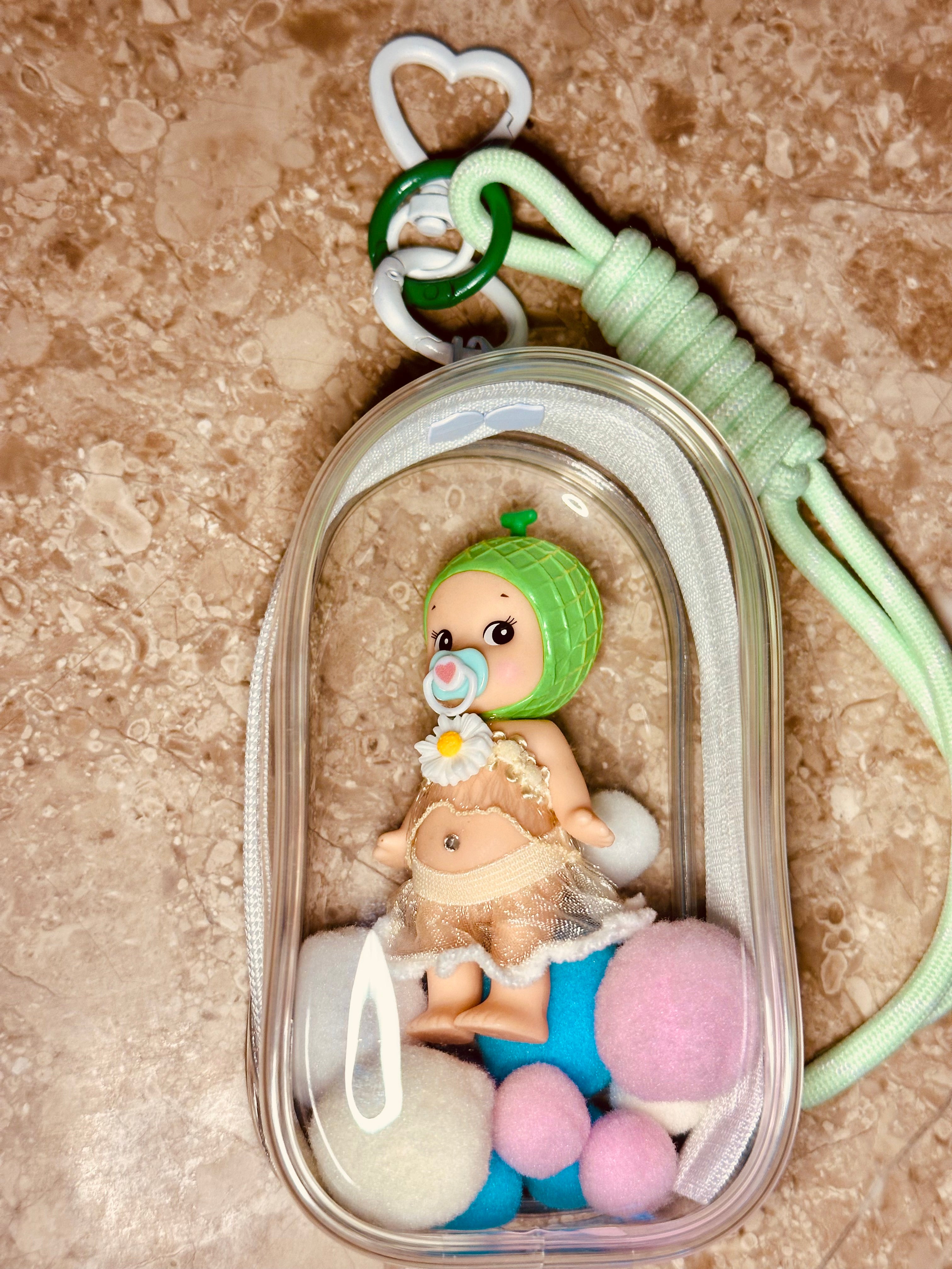 Keychain with a small figurine of a baby in a clear container on a textured surface