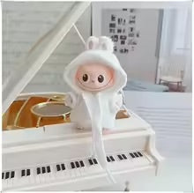Plush toy with a fWhite hoodie on a miniature piano in a room setting